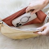 Person placing a phone into a beige handbag on a white fur surface