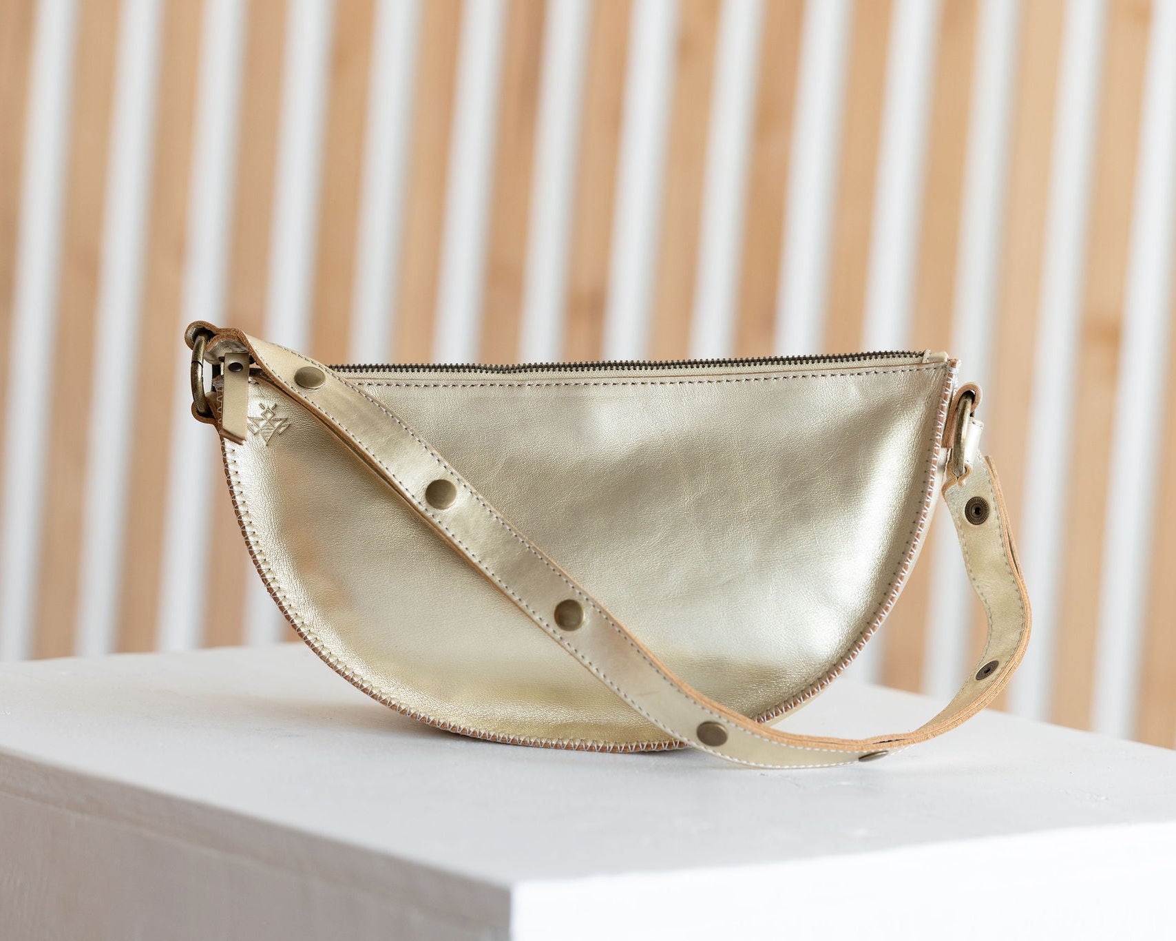 Gold handbag on a white surface with a beige curtain background