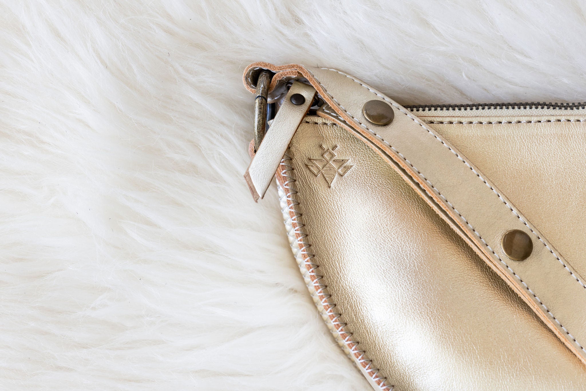 Close-up of a beige leather clutch with a brand logo on a white fur background