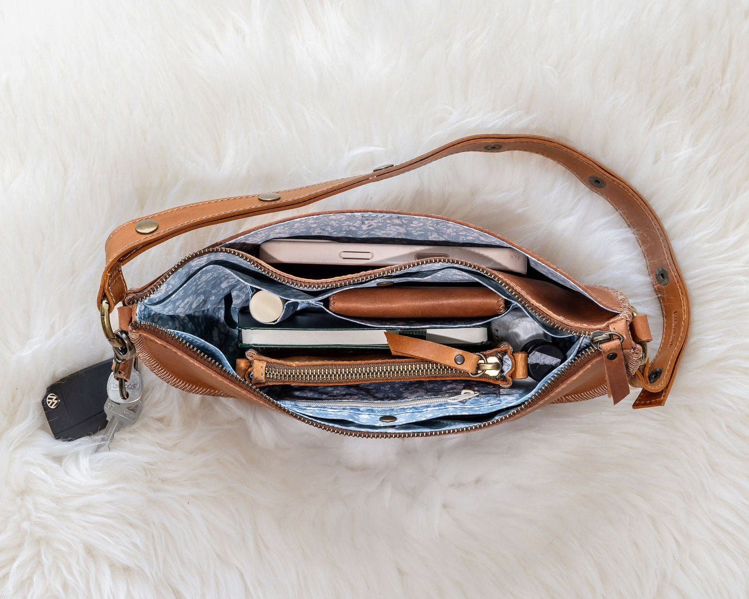 Open brown leather bag with items on a white fluffy surface