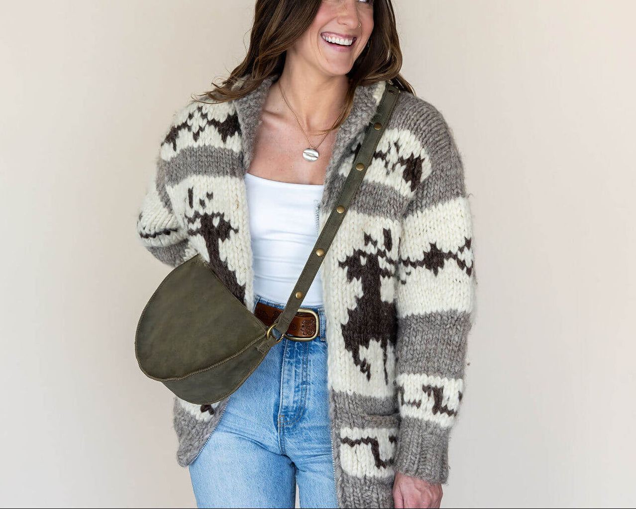 Woman wearing a patterned cardigan with a green bag against a plain background