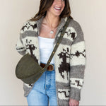 Woman wearing a patterned cardigan with a green bag against a plain background