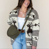 Woman wearing a patterned cardigan with a green bag against a plain background