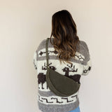 Person wearing a patterned sweater with a green bag over one shoulder against a plain background