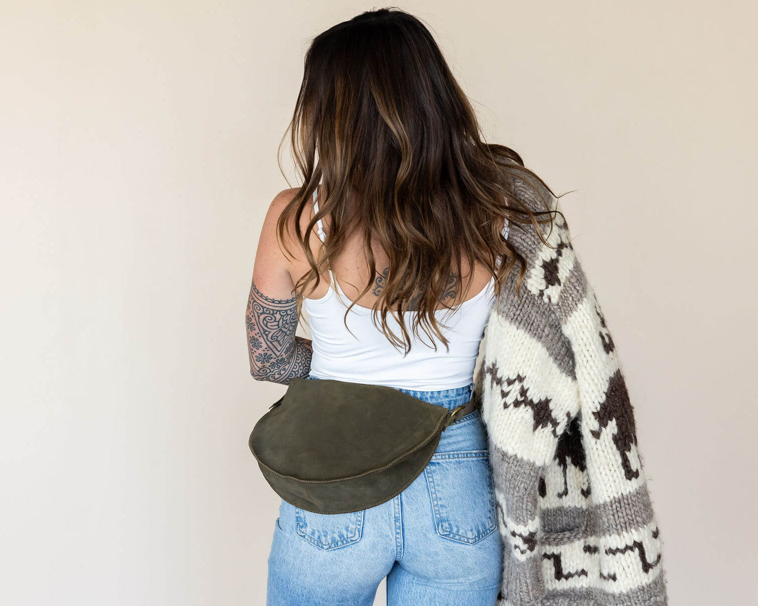 Woman wearing a patterned cardigan and carrying a green bag against a plain background