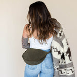 Woman wearing a patterned cardigan and carrying a green bag against a plain background