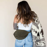 Woman wearing a patterned cardigan and carrying a green bag against a plain background