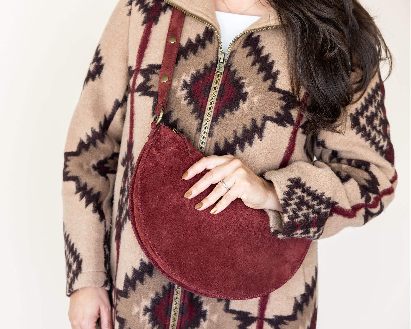 Person wearing a patterned coat holding a red handbag against a white background