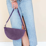 Person wearing a beige sweater, blue jeans, and brown boots with a purple handbag.
