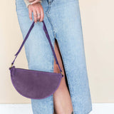 Person wearing a beige sweater, blue jeans, and brown boots with a purple handbag.