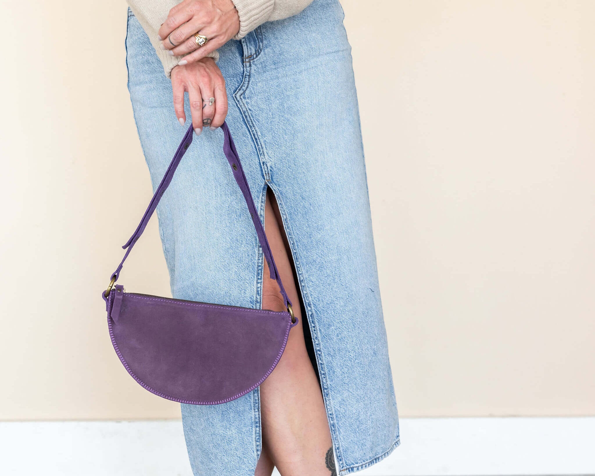 Person wearing a beige sweater, blue jeans, and brown boots with a purple handbag.
