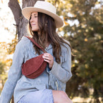Woman sitting on a wooden fence wearing a light blue coat, red boots, and a beige hat in a natural setting.