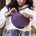 Woman holding a purple round bag outdoors with trees in the background