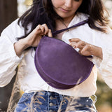 Woman holding a purple round bag outdoors with trees in the background