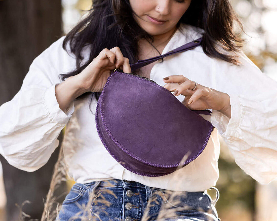 Woman holding a purple round bag outdoors with trees in the background