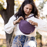 Woman holding a purple bag outdoors with trees in the background