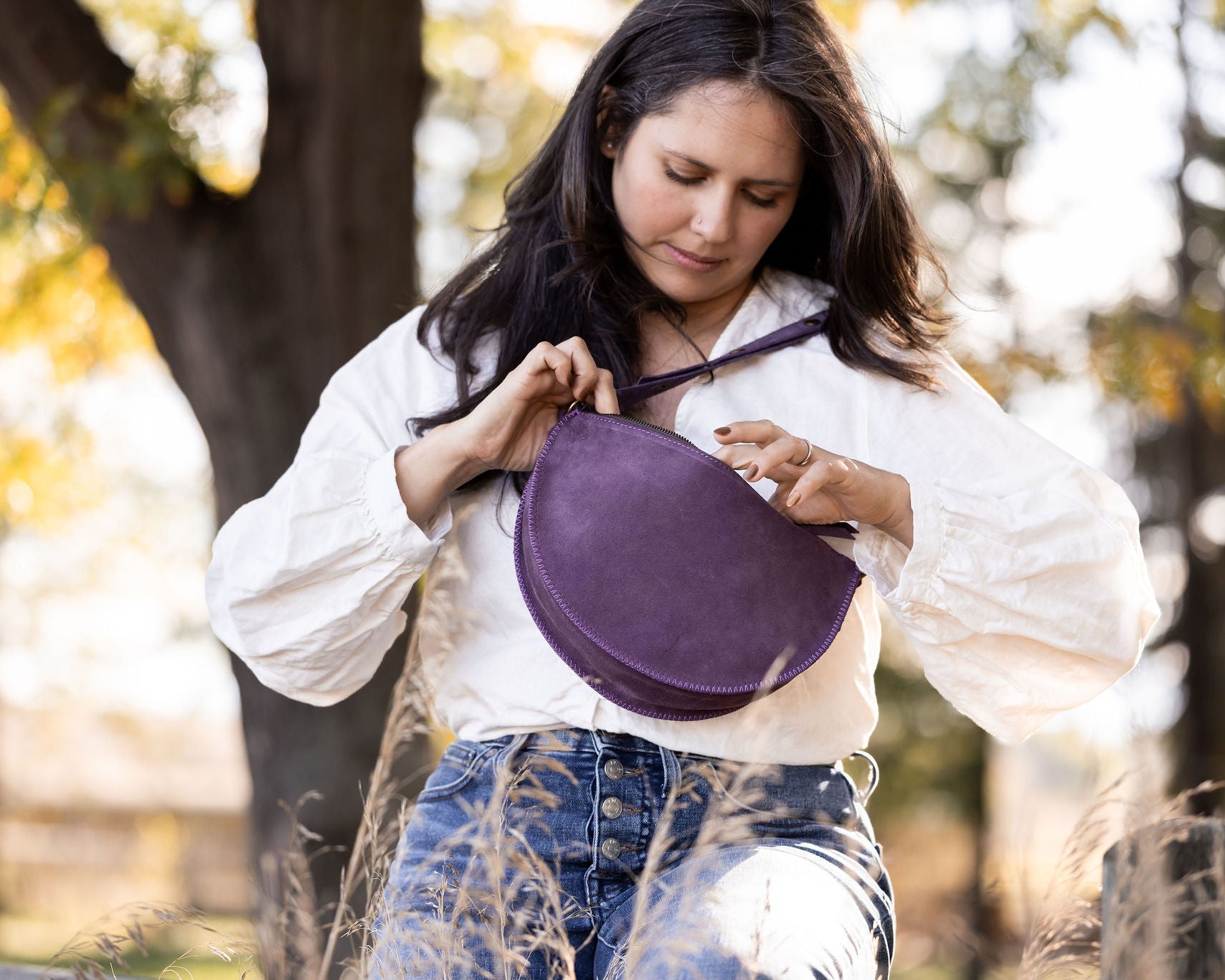Woman holding a purple bag outdoors with trees in the background