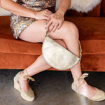 Person sitting on a brown couch holding a gold handbag, wearing a patterned dress and beige shoes.