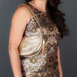 Woman wearing a patterned dress with a gold handbag against a gray background