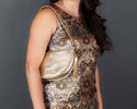 Woman wearing a patterned dress with a gold handbag against a gray background