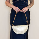 Person holding a gold handbag against a plain background