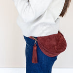 Person wearing a white sweater and blue jeans with a red suede bag on a beige background