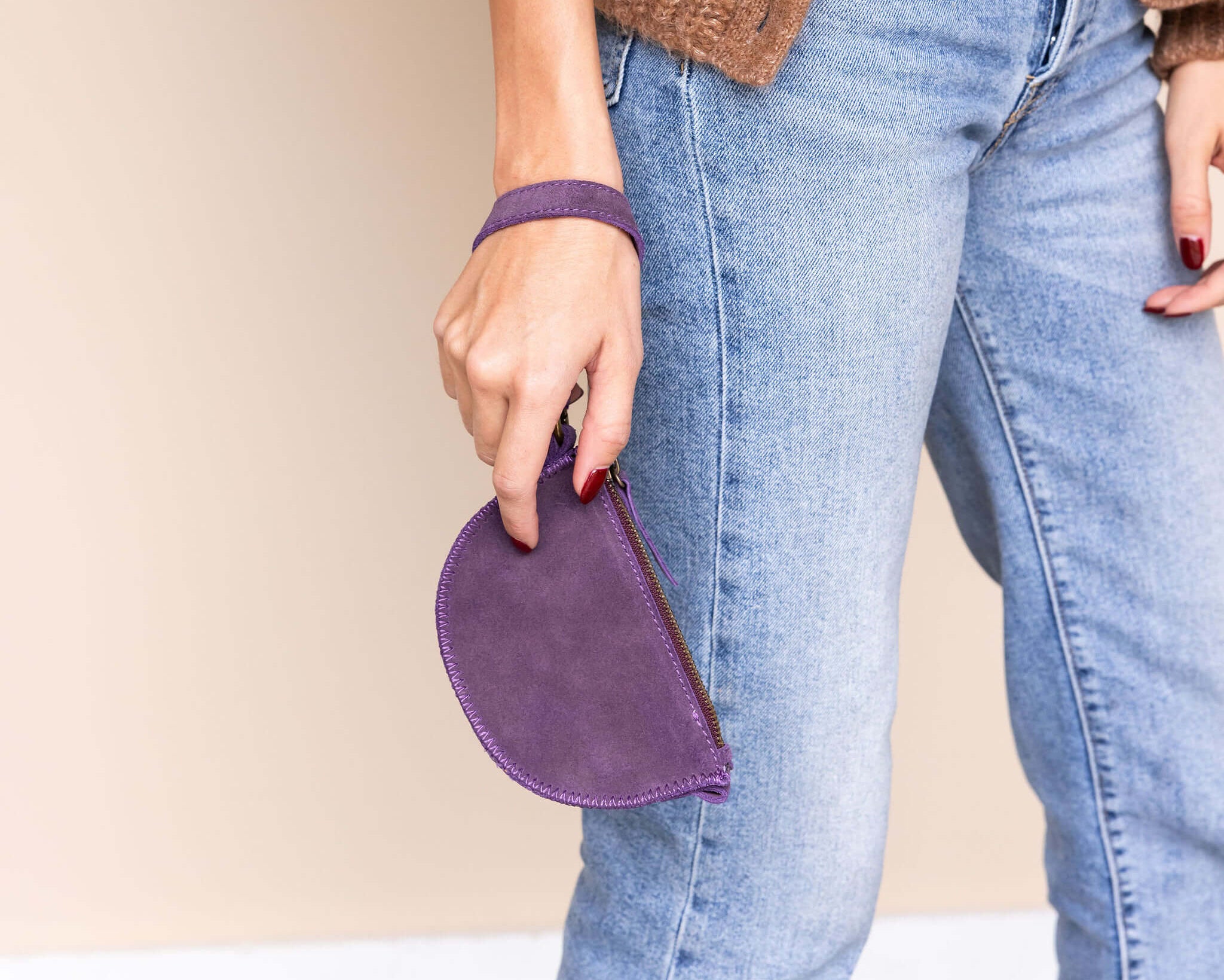 Person wearing a brown cardigan and blue jeans, holding a purple pouch against a neutral background