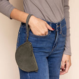 Person wearing a gray long-sleeve shirt and blue jeans with a green crossbody bag against a beige background