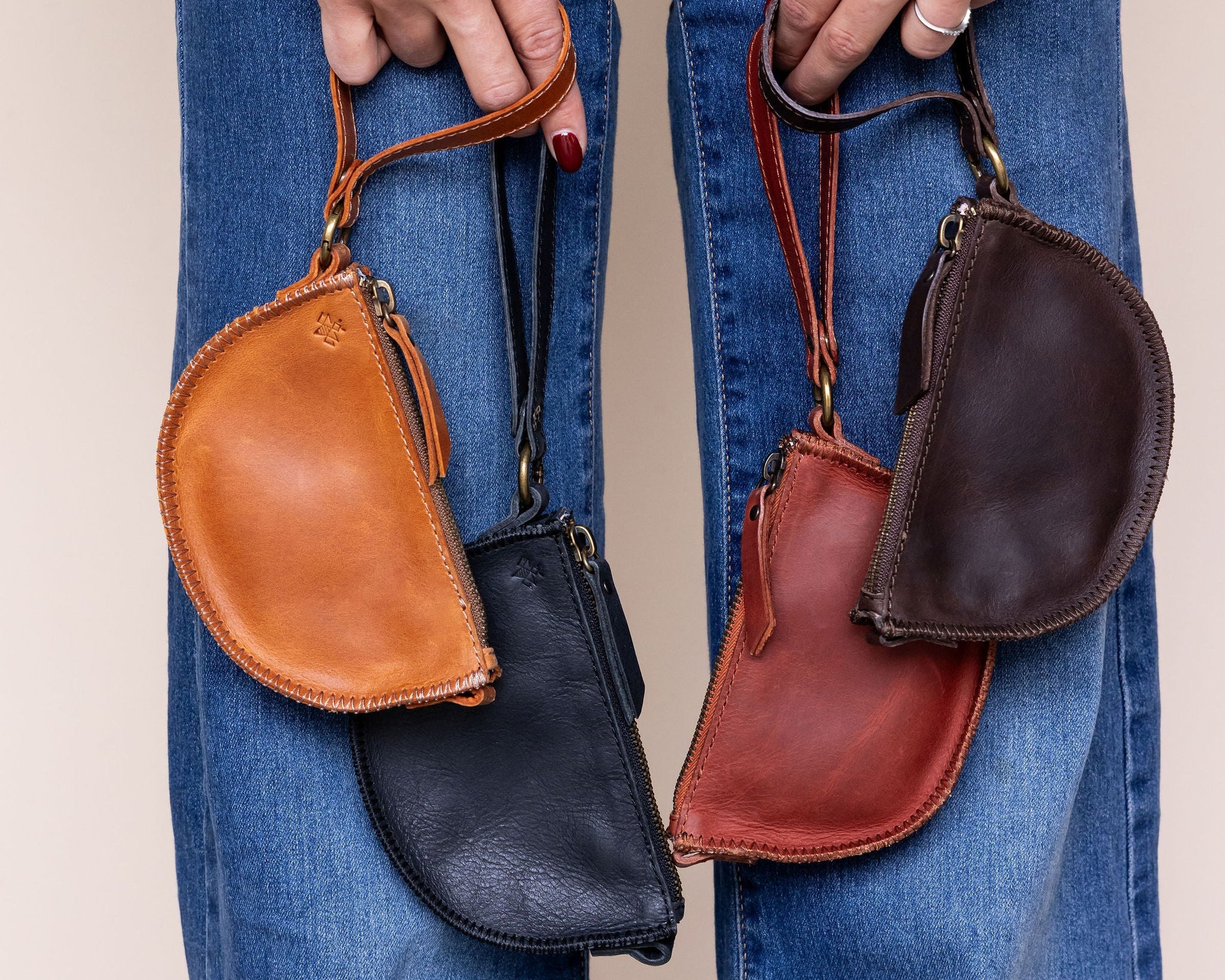 Person holding four leather pouches of different colors against a neutral background