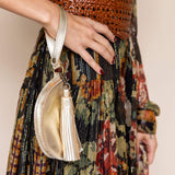 Person wearing a patterned dress holding a gold handbag with a tassel on a plain background