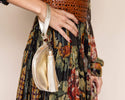 Person wearing a patterned dress holding a gold handbag with a tassel on a plain background