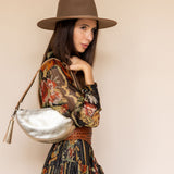 Woman wearing a patterned dress, brown hat, and holding a silver handbag against a beige background
