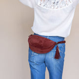 Person wearing a white sweater with floral details and blue jeans, carrying a red waist bag.