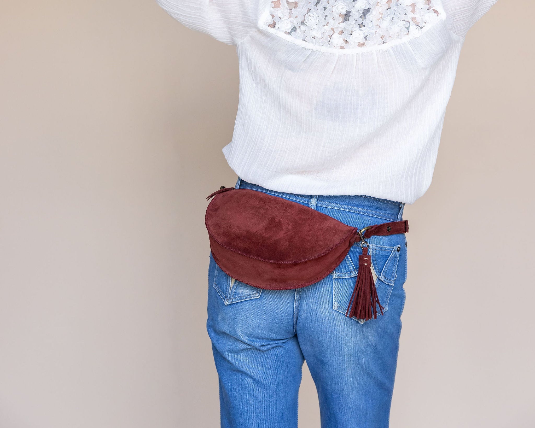 Person wearing a white sweater with floral details and blue jeans, carrying a red waist bag.