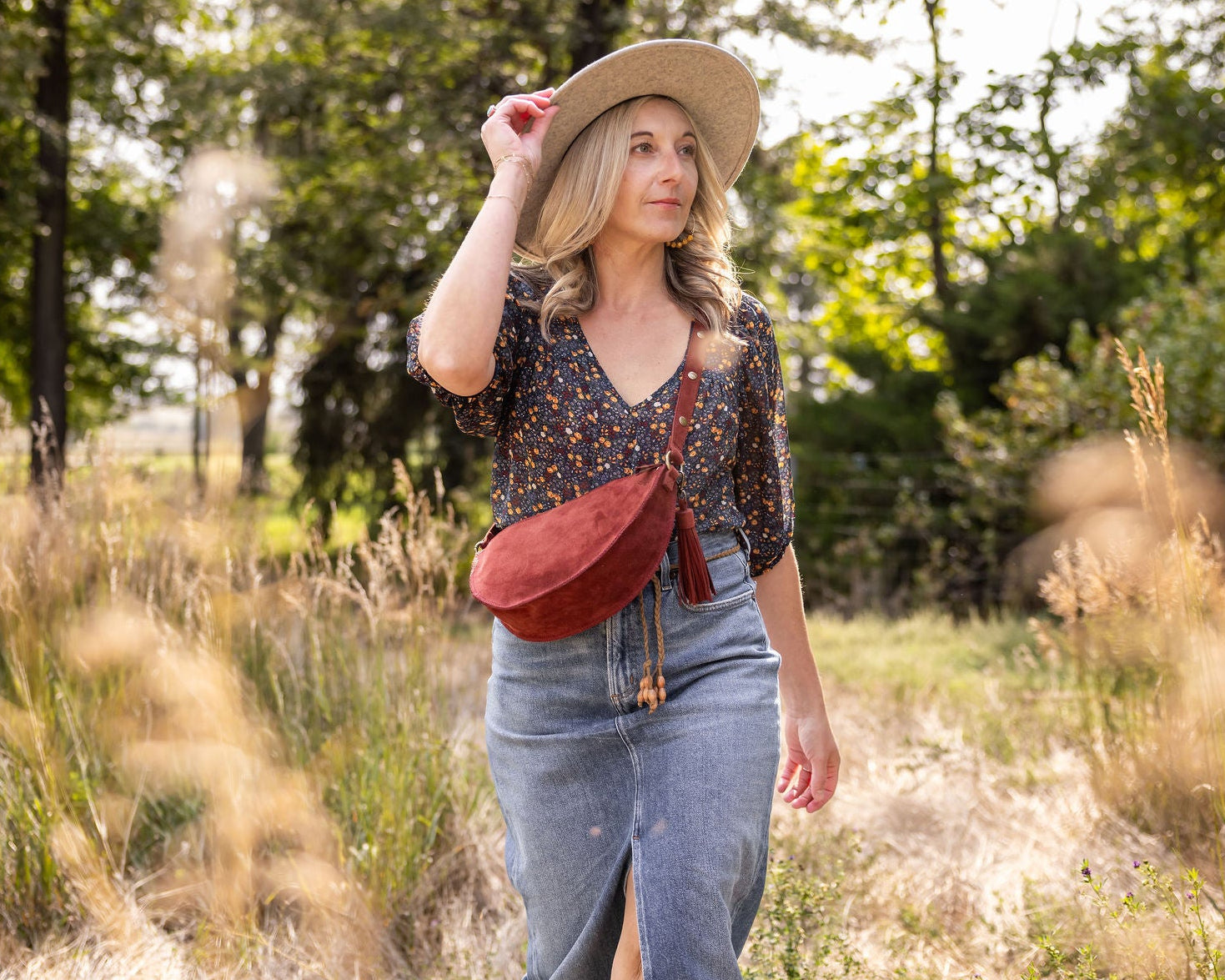 Woman in a field wearing a straw hat and carrying a red crossbody bag.