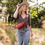 Woman in a field wearing a straw hat and carrying a red crossbody bag.