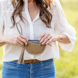 Woman holding a beige belt bag with a blurred natural background