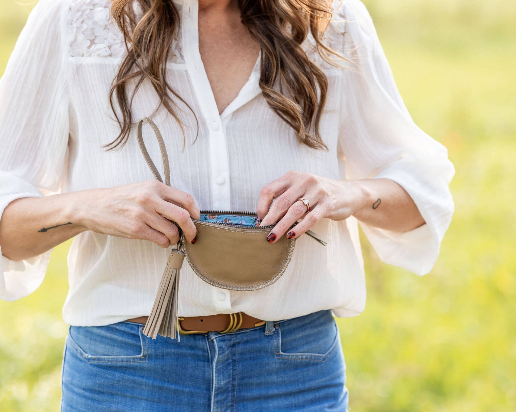 Woman holding a beige belt bag with a blurred natural background