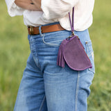 Person wearing a white blouse, blue jeans, and a brown belt with a purple bag in a grassy field.