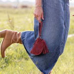 Person wearing blue jeans and brown boots with a red bag in a grassy field