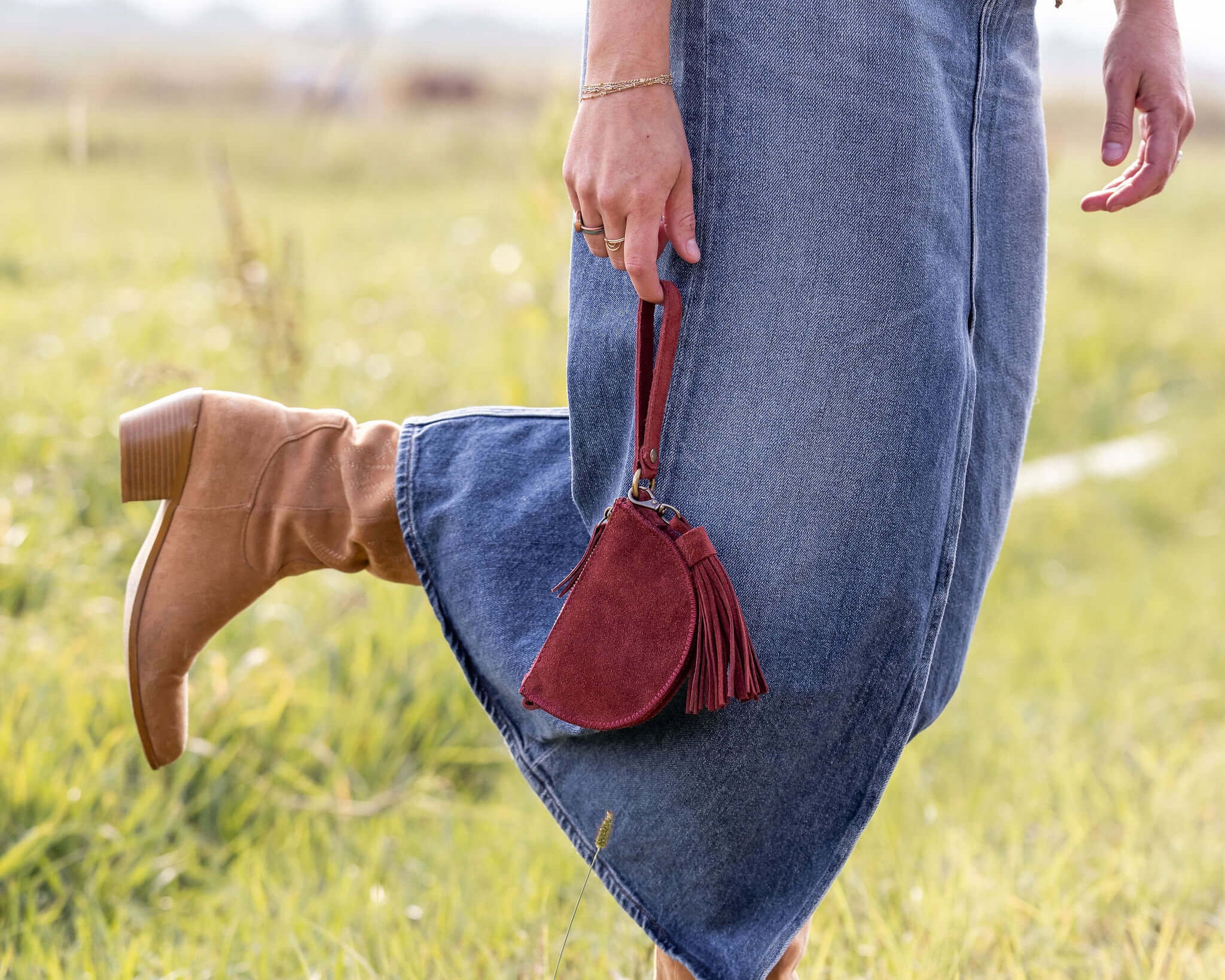 Person wearing blue jeans and brown boots with a red bag in a grassy field
