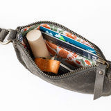 Gray waist bag with items including a candle, cards, and a small container on a white background