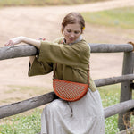 Woman wearing the Woven Terracotta & Seashell Biggie Bee crossbody in a mountain field