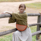 Woman wearing the Woven Terracotta & Seashell Biggie Bee crossbody in a mountain field
