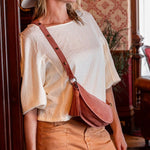 Woman in a white blouse and tan pants standing in a room with wooden paneling and a chandelier.