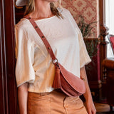 Woman in a white blouse and tan pants standing in a room with wooden paneling and a chandelier.