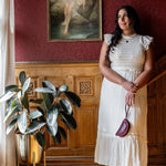 Woman in a white dress standing in a room with red walls and a painting of a cow.