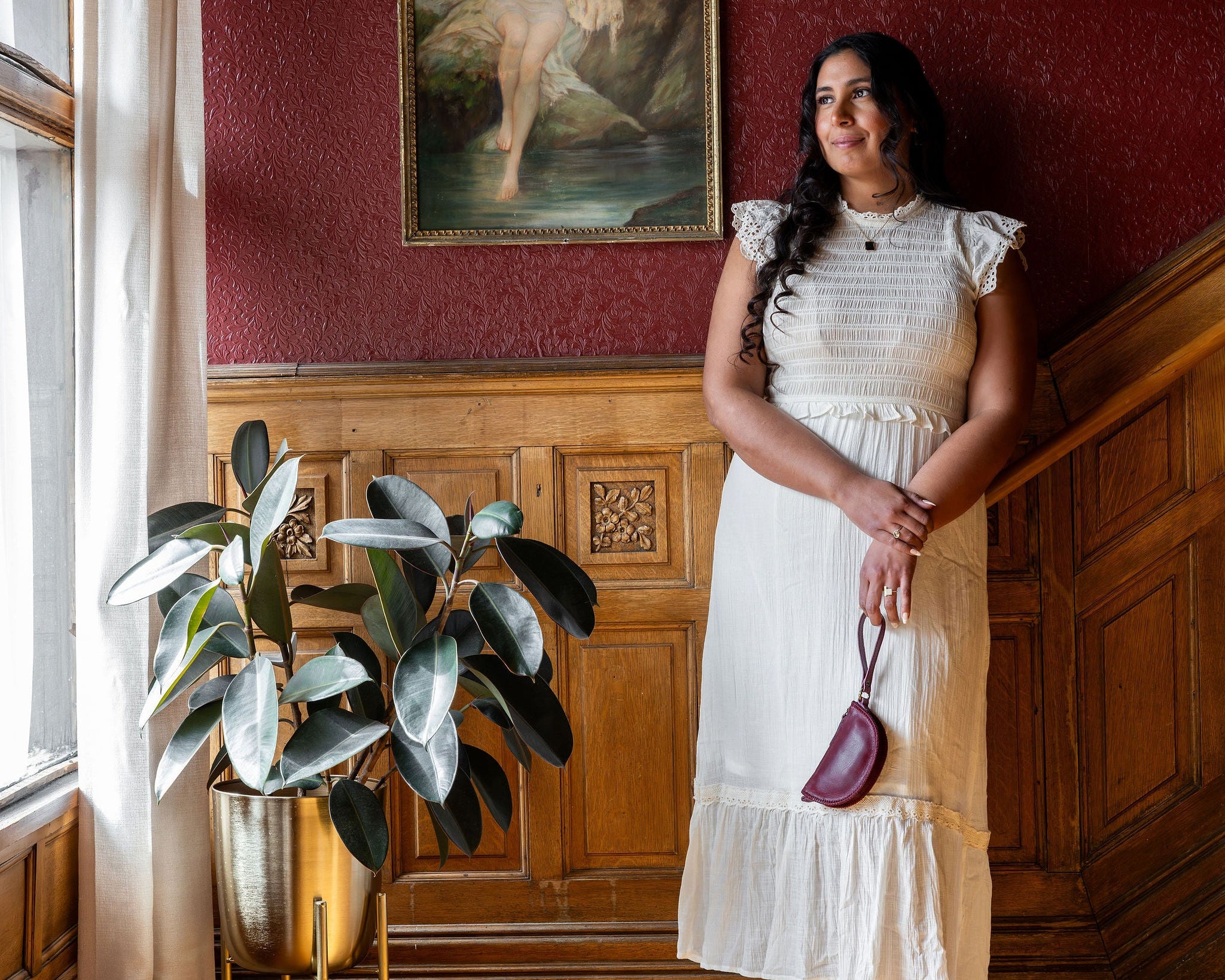 Woman in a white dress standing in a room with red walls and a painting of a cow.