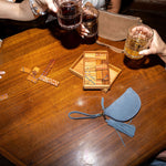 Two people enjoying drinks at a wooden table with board games and a small bag.