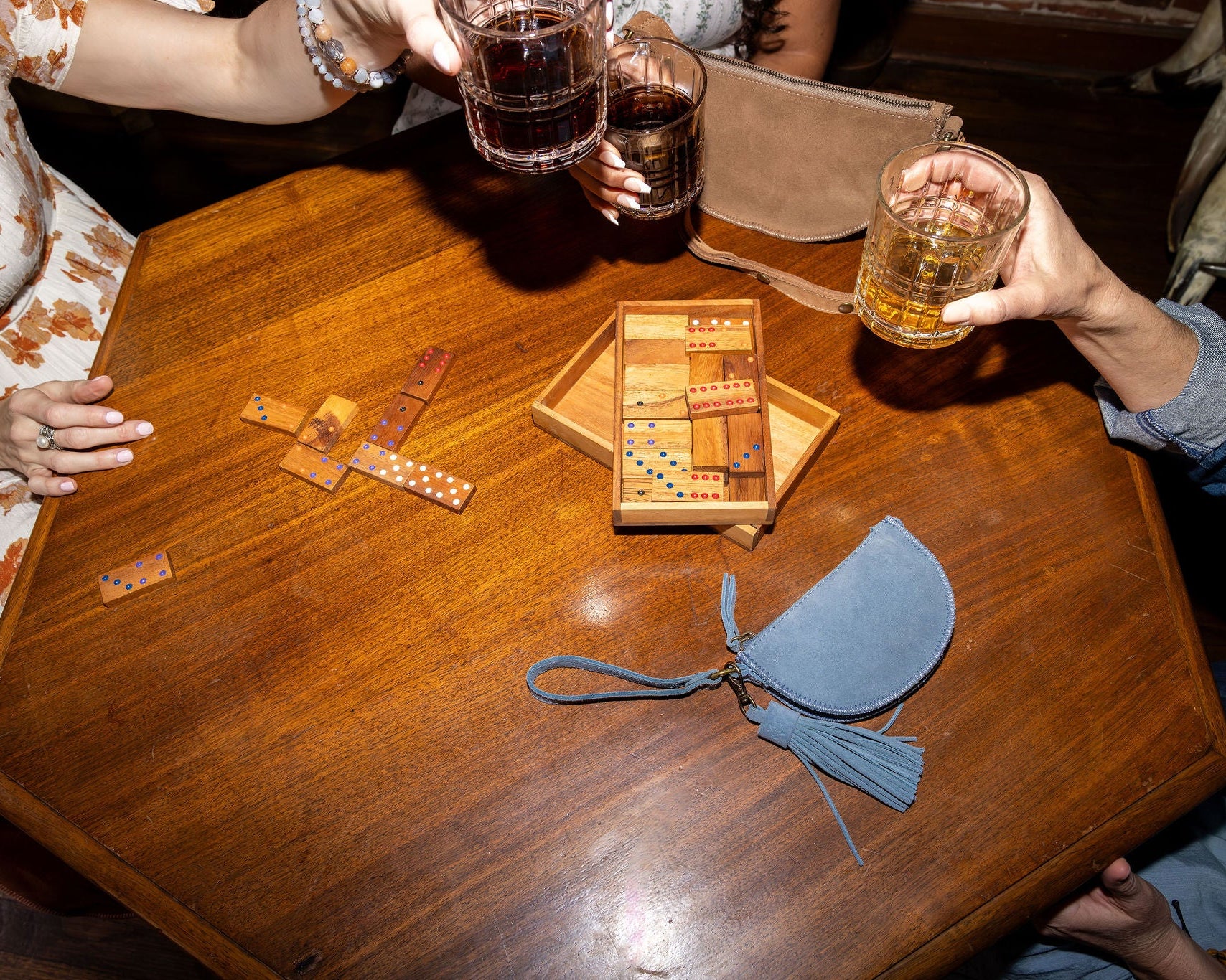 Two people enjoying drinks at a wooden table with board games and a small bag.